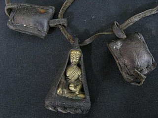 Nahaufnahme des bronzenen Buddha im Lederanhänger, mit weiteren Lederbeuteln im Hintergrund