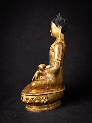 Nepali bronze Buddha statue in side profile, seated with right hand reaching down