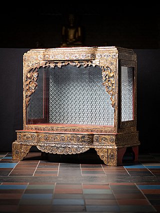 Burmese wooden temple shrine in three-quarter view showing gilded carvings and side glass panel
