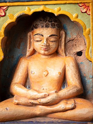 Close-up van het gezicht en bovenlichaam van het Jain-beeld in de nis, met beschilderde boogrand