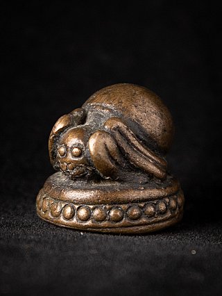 Burmese bronze opium weight with reclining animal figure on a round base, three-quarter view