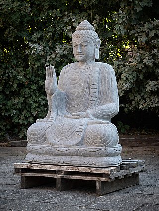 Indonesian stone Buddha statue, three-quarter view showing raised right hand and robe folds