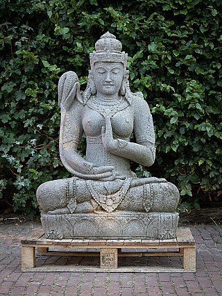 Dewi Sri lavastone statue from Indonesia, seated on a plinth, full front view
