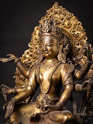 Three-quarter close-up of a gilt-bronze Vasudhara, crown and halo in view