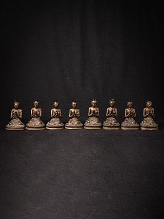 Eight Burmese bronze monk statues in a straight row, frontal view with hands in prayer
