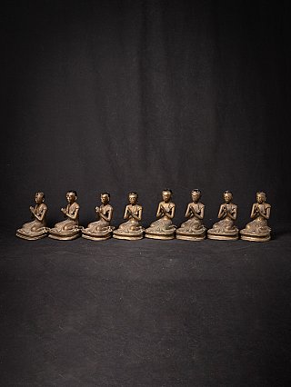 Eight Burmese bronze monk statues lined up at an angle, showing partial side profiles