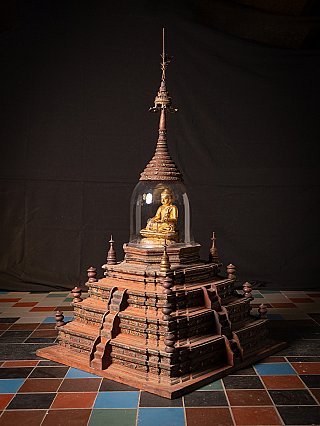 Burmese wooden stupa with tiered base and glass dome around the gilded Buddha figure, angled front view