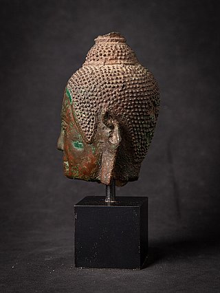 Bronzen Boeddhahoofd Thailand, zijaanzicht links met lang oor en krulhaar, op sokkel