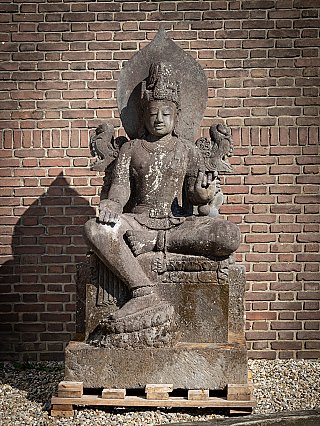 Avalokiteshvara statue in Indonesian lavastone, seated on plinth with halo-like back slab, front view