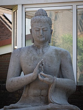 Upper body of an Indonesian lavastone Buddha statue with dharmachakra mudra, front view