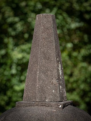 Finial detail of the lavastone stupa, showing coarse stone texture and light surface deposits
