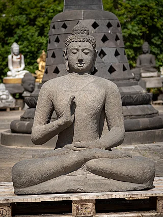 Buddha statue in Indonesian lava stone, seated full-front with raised right hand