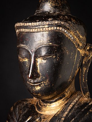 Close-up face detail of the Burmese wooden Buddha with patina and gilding traces
