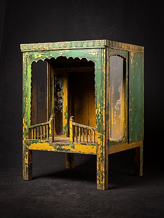 Antique wooden Indian temple shrine in three-quarter view, open front with worn green and yellow paint
