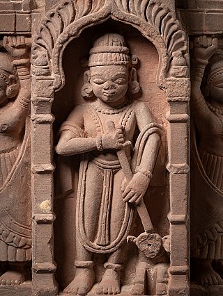 Close-up of the standing main figure under the arch with staff and jewellery