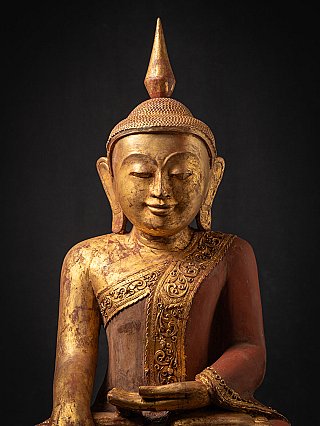 Face detail of Burmese wooden Buddha with gilding, elongated ears and red robe