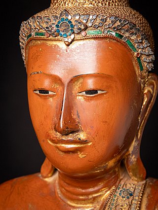 Face close-up of Burmese wooden Buddha with half-closed eyes and worn gilding