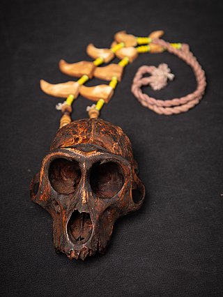 Wooden monkey skull with Naga necklace laid behind it, cord and beads visible