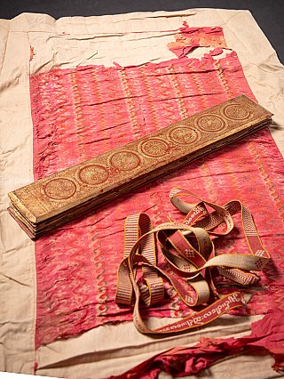 Kammavaca manuscript with red cover on pink textile, with loose tying ribbons