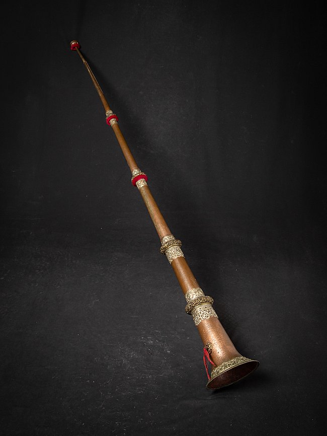 Tibetan copper dungchen horn, angled view with engraved metal bands and red rings