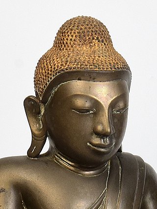 Face detail of a Burmese bronze Buddha with elongated earlobe and textured hair curls