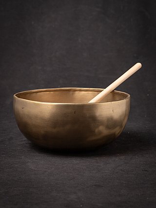 Nepali bronze singing bowl with wooden mallet resting inside, angled view