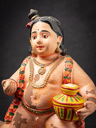 Krishna child statue detail showing face and striped pot, three-quarter view