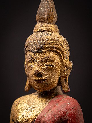 Face detail with gilded surface and red lacquer robe over the shoulder of the wooden statue
