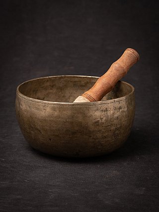 Antique Nepali bronze singing bowl with wooden striker resting inside, three-quarter view