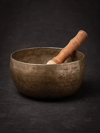 Antique Nepali bronze singing bowl with wooden striker resting inside, three-quarter view