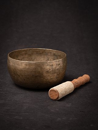 Bronze singing bowl from Nepal with striker placed beside it, angled view