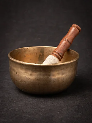 Antique Nepali bronze singing bowl with striker resting inside, angled view