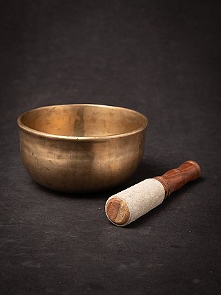 Nepali bronze singing bowl with striker beside it on cloth backdrop, three-quarter view