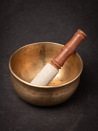 Bronze singing bowl from Nepal with striker inside the bowl, angled top view