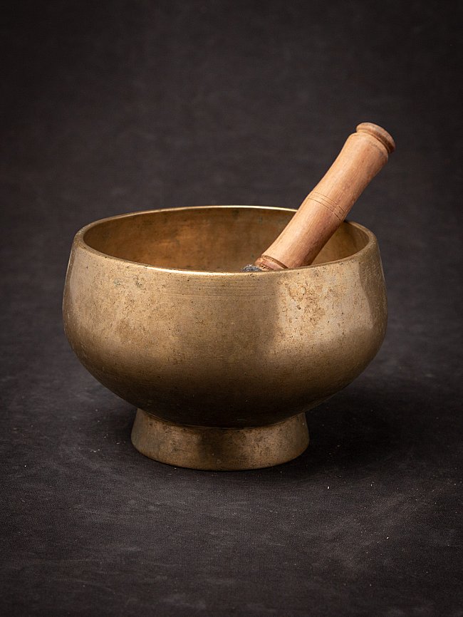Nepali bronze singing bowl with wooden striker resting inside, three-quarter view