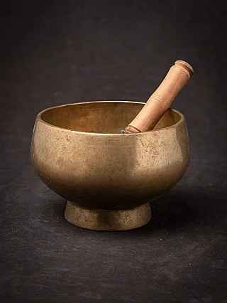Nepali bronze singing bowl with wooden striker resting inside, three-quarter view