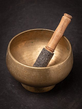 Nepali bronze singing bowl with striker leaning in the bowl, top angled view
