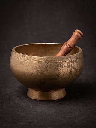 Nepali bronze singing bowl with wooden striker resting inside, angled full view