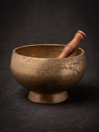 Nepali bronze singing bowl with wooden striker resting inside, angled full view