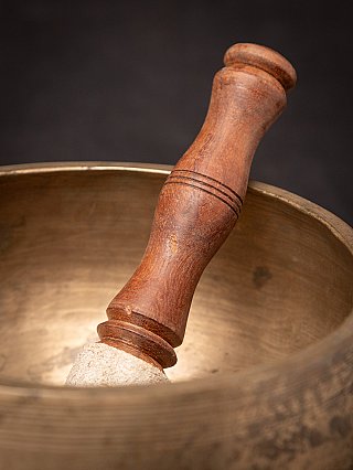 Wooden striker with turned handle resting in the Nepali singing bowl, close-up