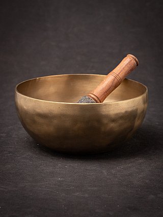 Nepali bronze singing bowl with wooden striker resting inside, angled view