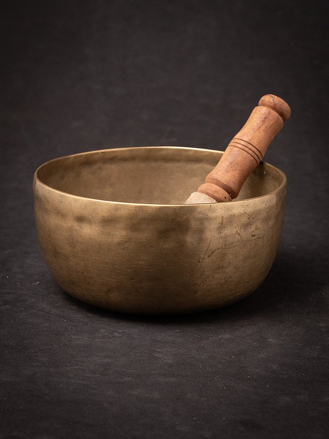Nepalese bronzen klankschaal met houten klopper, schuin in de schaal op donkere ondergrond