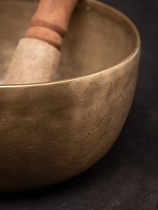 Detail van de bronzen klankschaal met de klopper op de achtergrond, focus op krassen en patina