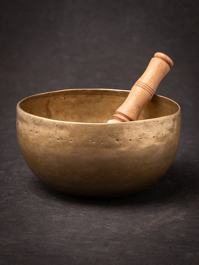 Nepali bronze singing bowl with wooden striker resting inside, angled view
