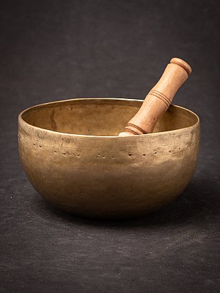 Nepali bronze singing bowl with wooden striker resting inside, angled view