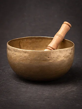 Nepali bronze singing bowl with wooden striker resting inside, angled view