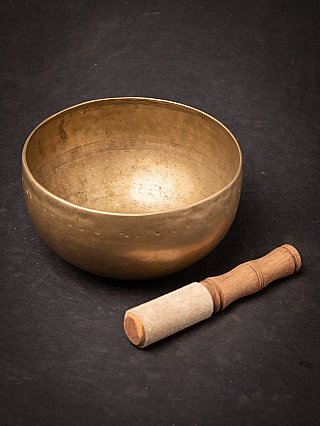 Nepali bronze singing bowl with separate striker beside it, slightly top-down view