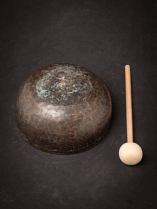Onderzijde van de Nepalese bronzen klankschaal met patina, met klopper ernaast