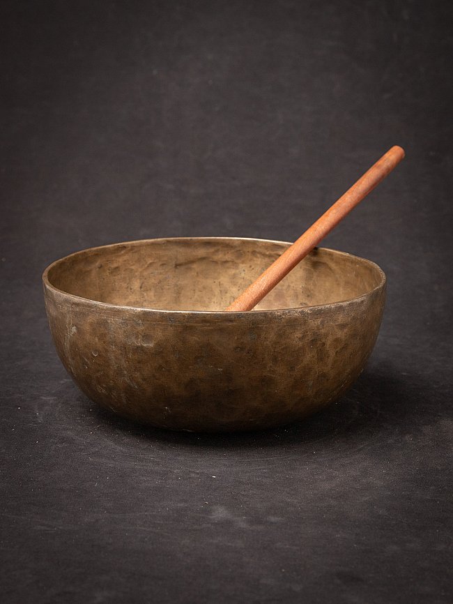 Nepali bronze singing bowl with wooden mallet resting inside, three-quarter view