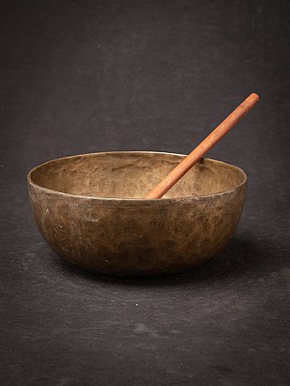 Nepali bronze singing bowl with wooden mallet resting inside, three-quarter view